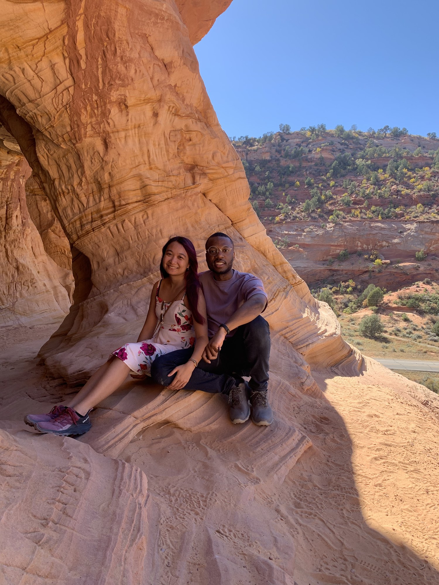 Krishel and Omar sit together under a sandstone arch in the desert.